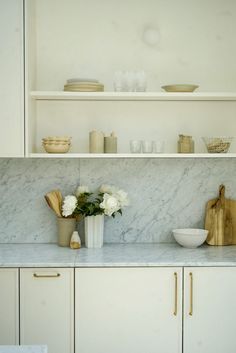 a white kitchen with marble counter tops and shelves filled with plates, bowls, and utensils