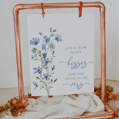 a card with blue flowers on it sitting in front of a white background and copper frame