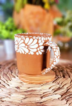 a brown and white coffee cup sitting on top of a woven place mat next to a potted plant