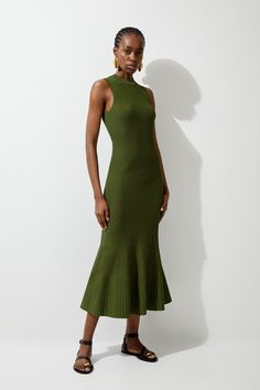 a woman standing in front of a white wall wearing a green dress