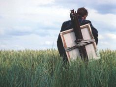 a man holding an old tv in a field with tall grass and blue sky behind him