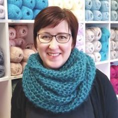 a woman wearing glasses standing in front of shelves with crocheted scarves on them