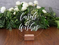 a clear acrylic sign that says cards and wishes on it with white flowers in the background