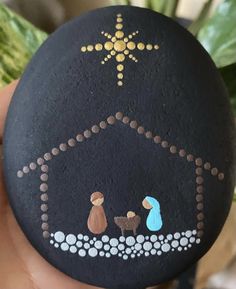 a hand holding a painted rock with a nativity scene on it's side