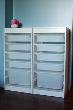 two white storage cabinets with plastic containers on top and one has a pink flower in the middle