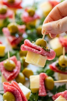 a person holding a piece of food with olives and cheese on it, in front of other appetizers