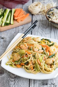 shrimp and vegetable stir fry on a white plate with chopsticks next to it