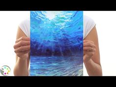 a woman holding up a painting with blue water