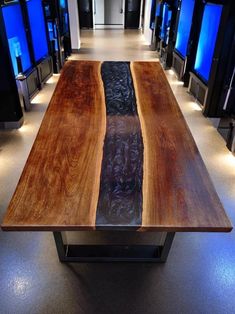 a wooden table sitting in the middle of a room with blue televisions behind it