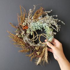 someone is holding a wreath made out of dried plants and twigs on a gray background