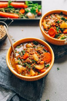 two bowls of soup with carrots, potatoes and lentils on a table top