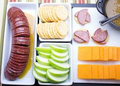 an assortment of meats, cheese and fruit are arranged on trays next to a bowl of soup