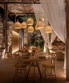 an outdoor dining area with wooden tables and chairs, hanging lights and curtains over them