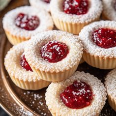 small pastries with powdered sugar and jelly toppings are on a brown plate