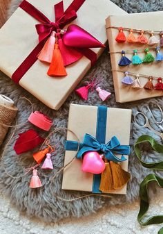 four wrapped presents with tassels and bows on a gray rug next to twine spools