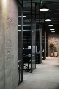 an office with glass partitions and black walls is lit by recessed light fixtures