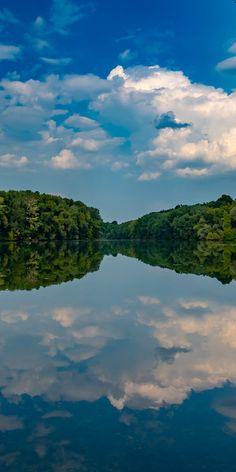 the sky is reflected in the still water on the lake's surface, with trees and bushes lining both sides