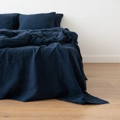 an unmade bed with dark blue linens on the bottom, and white walls in the background