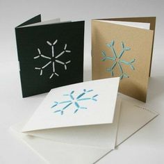 three cards with snowflakes on them are sitting next to each other, one is folded and the other has an envelope