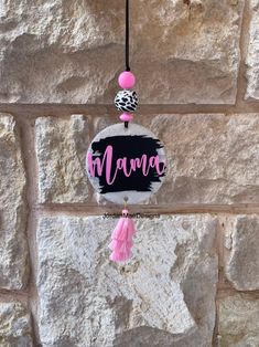 a sign hanging from the side of a stone wall next to a pink ball and tassel