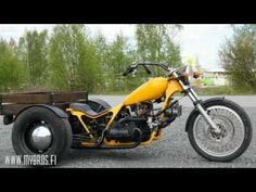 a yellow motorcycle parked next to a wooden trailer on gravel road with trees in the background