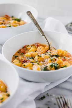 three white bowls filled with pasta and cheese on top of a table next to silverware