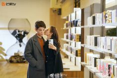 a man and woman standing next to each other in front of a book shelf filled with books