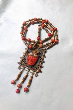 a necklace with red beads and an orange face on it's chain, hanging from a white background