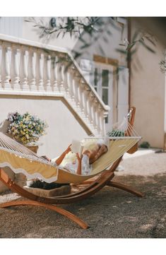 a woman laying in a hammock reading a book on the front steps of a house