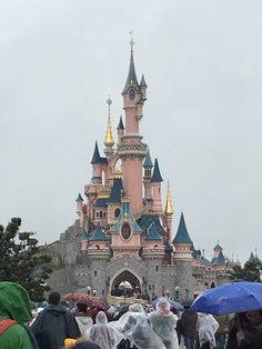 people walking in front of a castle with umbrellas on a cloudy day at disneyland