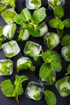 ice cubes and mint leaves on a black table top, with water in the middle