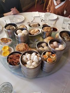 a group of people sitting around a round table with food on it and plates in front of them