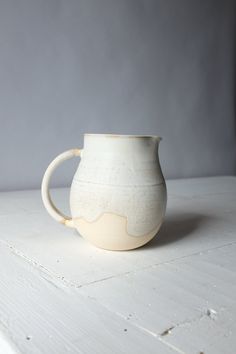 a white vase sitting on top of a wooden table next to a gray wall in the background