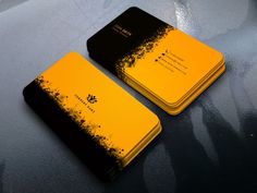 two yellow and black business cards sitting on top of a gray surface with ink splatters