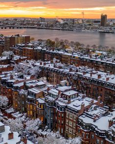 an aerial view of snow covered buildings and the water in the background at sunset or dawn