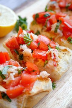 two pieces of bread with tomatoes and parsley on them next to lemon wedges