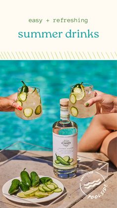 two people holding glasses with cucumber and gin on the table next to a pool