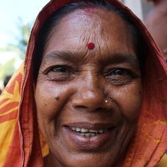 an old woman wearing a red and yellow sari with a smile on her face