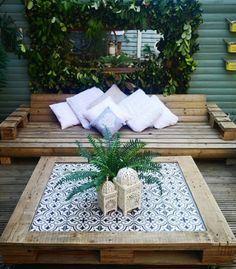 an outdoor table made out of pallets with pillows and plants in the middle on top