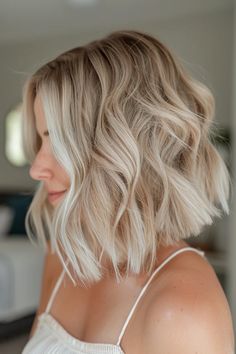 Woman with wavy, blonde bob hairstyle wearing a white top. Soft Beige Blonde Hair, Cream Blonde Hair Balayage, Blonde Bob With Lowlights, Dark Blonde Lob, Bob With Lowlights, Blonde Lob With Bangs, Dark Lowlights, Warm Blonde Balayage, Beige Blonde Hair Color