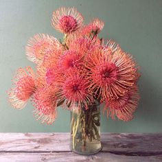 a vase filled with pink flowers sitting on top of a wooden table next to a green wall