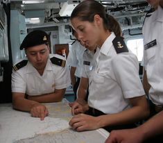 two sailors are looking at a map while others look on