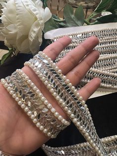 a woman's hand holding three bracelets with pearls on them and flowers in the background