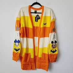 an orange and yellow striped cardigan with mickey mouse patches on the sleeves, hanging against a white wall