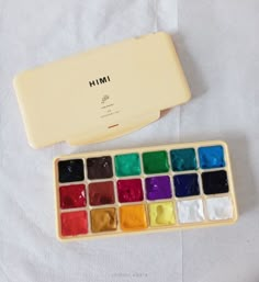 a box of paint sitting on top of a white sheet next to a brush and palette