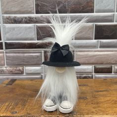 a doll with white hair wearing a black hat and slippers on a wooden table