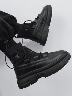 a pair of black boots with laces on them sitting on a white surface in front of a person's legs