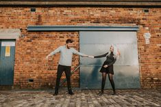 a man and woman standing in front of a brick building holding hands with each other