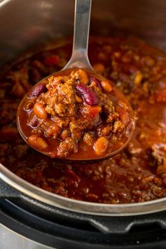 a ladle full of chili and beans is being held by a spoon