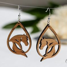 two wooden earrings with horses on them hanging from a clothes line next to a plant